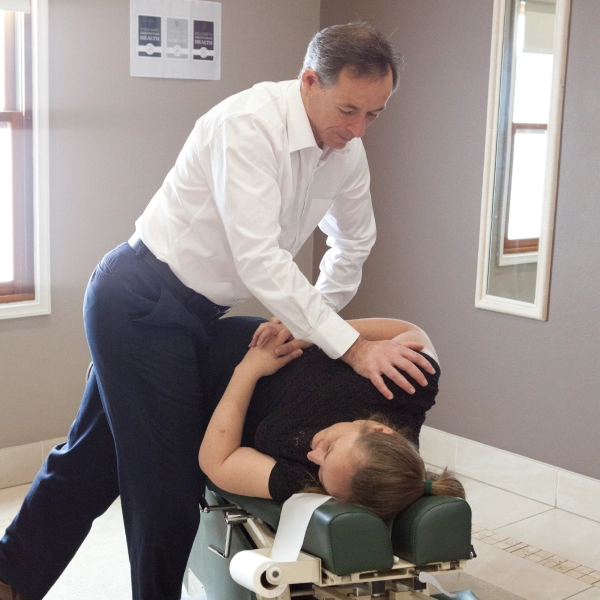 Dr Marcus Chacos delivering an adjustment to a patient lying face down on a drop table in the practice.